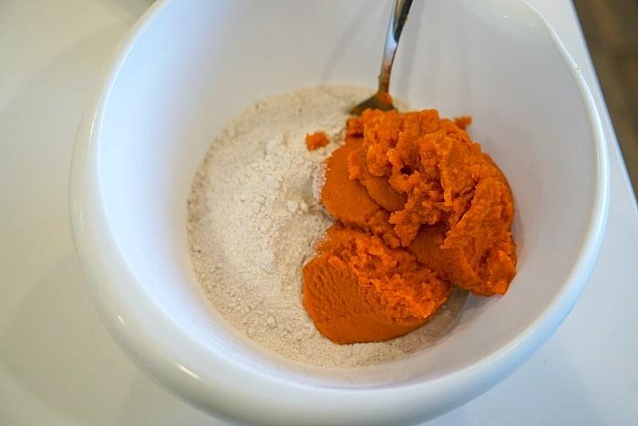 A white bowl holds a simple mix of cake mix and vibrant orange pumpkin puree, with a metal spoon ready to stir. Perfect for crafting fluffy 2-ingredient pumpkin muffins.