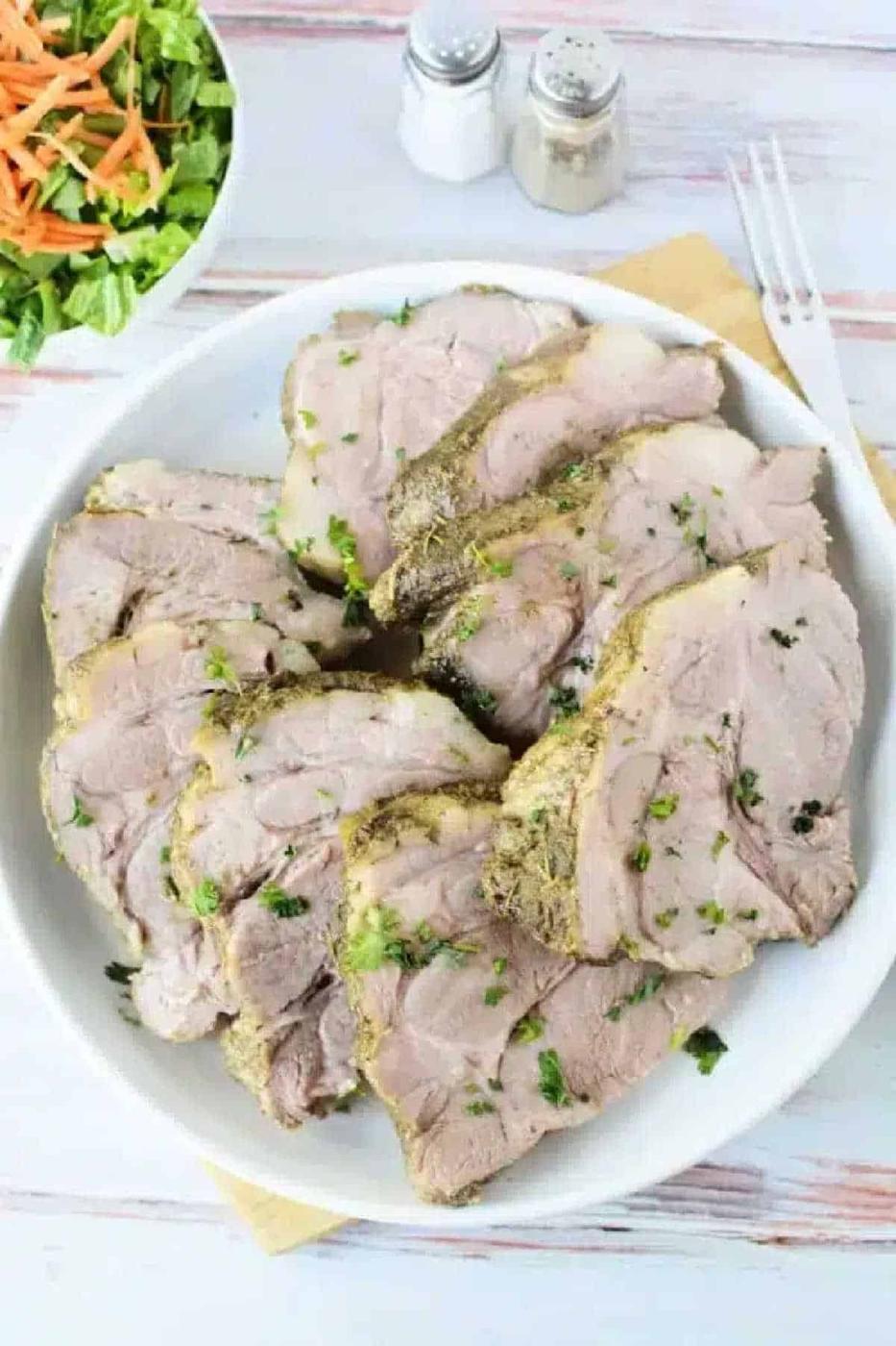 Sliced herb-crusted 3 Ingredient Pork Roast Slow Cooker on a white plate, served with a fresh salad and salt and pepper shakers in the background.