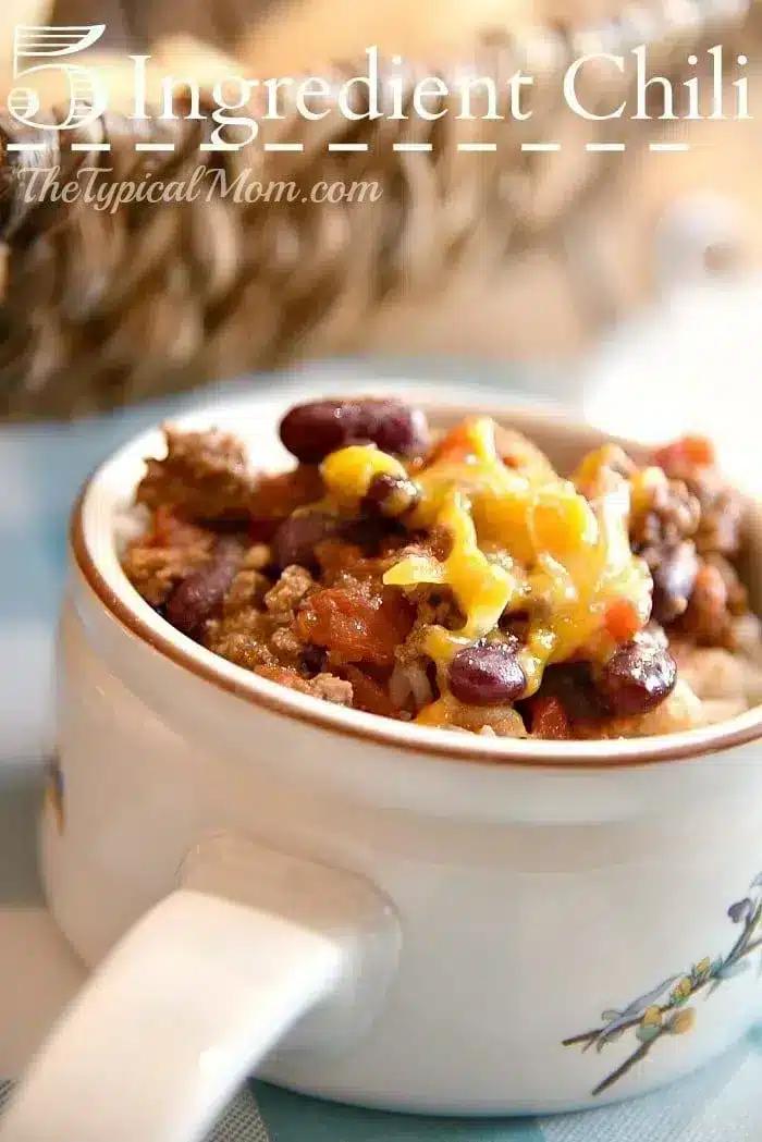 A close-up of a bowl of 5 ingredient crockpot chili recipe is shown. The chili consists of ground meat, beans, tomatoes, and is topped with shredded cheese.