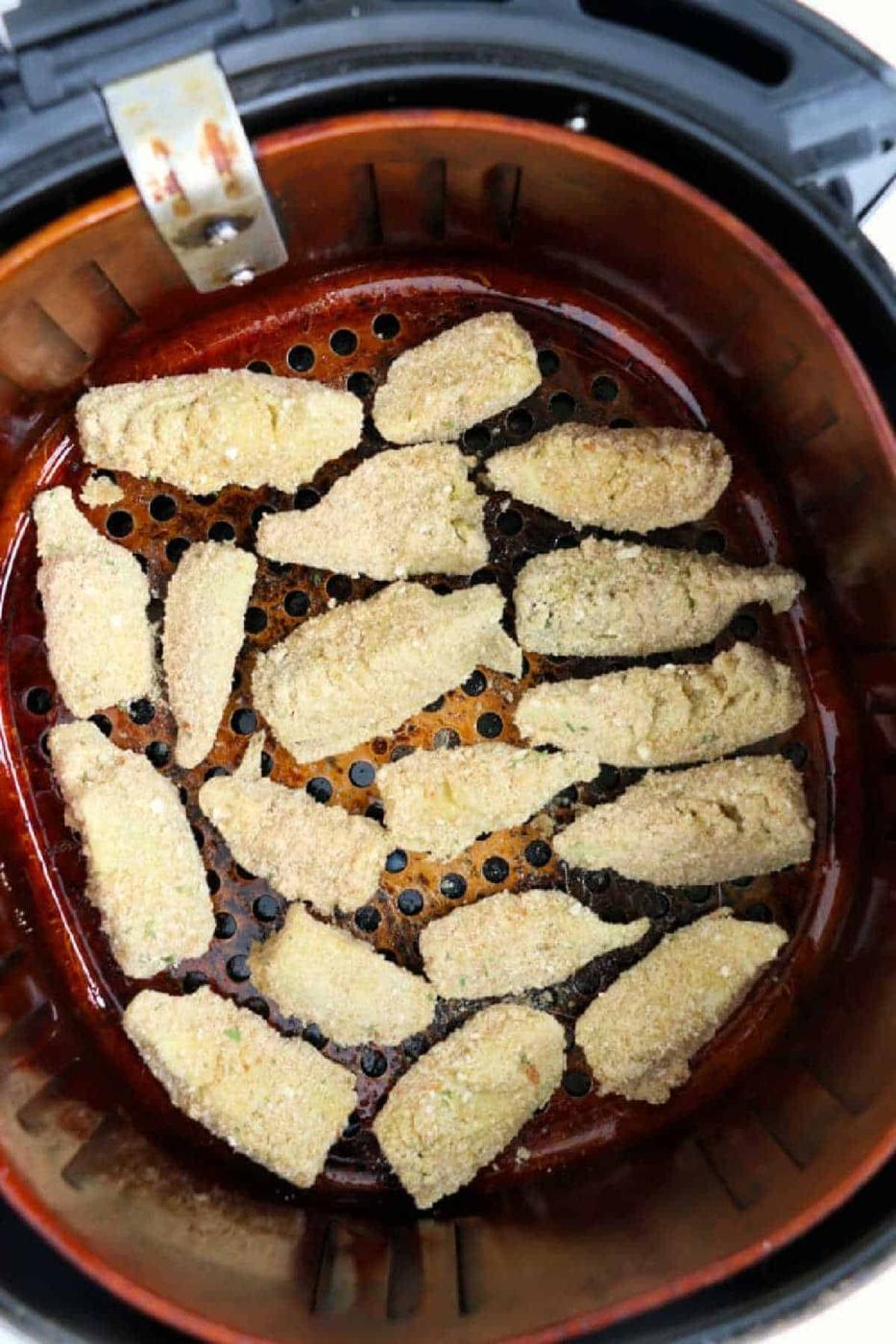 Breaded zucchini slices arranged in a single layer inside an air fryer basket, ready to be cooked—perfect alongside air fryer artichoke hearts for a tasty appetizer spread.