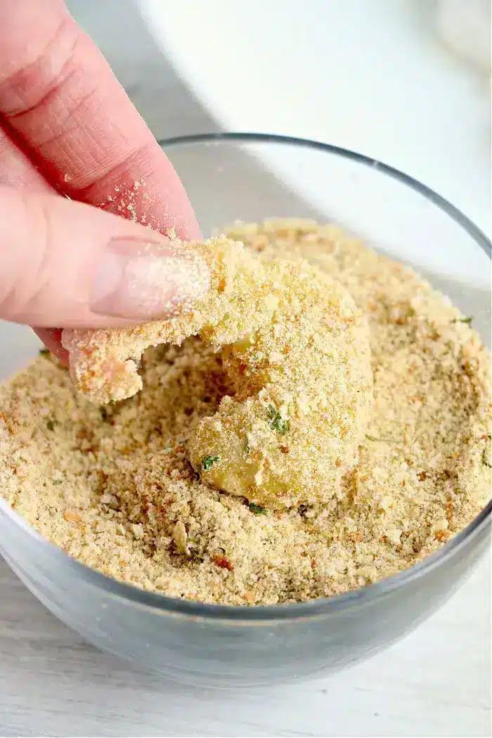 A hand coating a shrimp in seasoned breadcrumbs inside a glass bowl, prepping it for crispy air fryer bang bang shrimp.