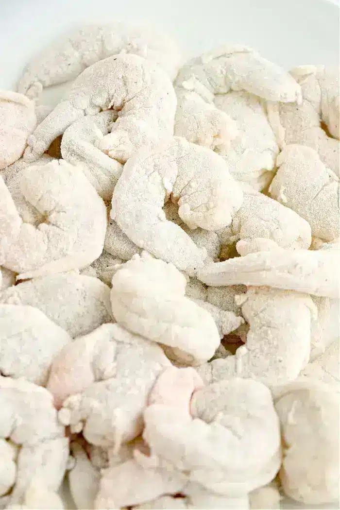 Frozen, uncooked shrimp piled together, covered in a light layer of frost on a white surface—perfect for making crispy air fryer bang bang shrimp at home.