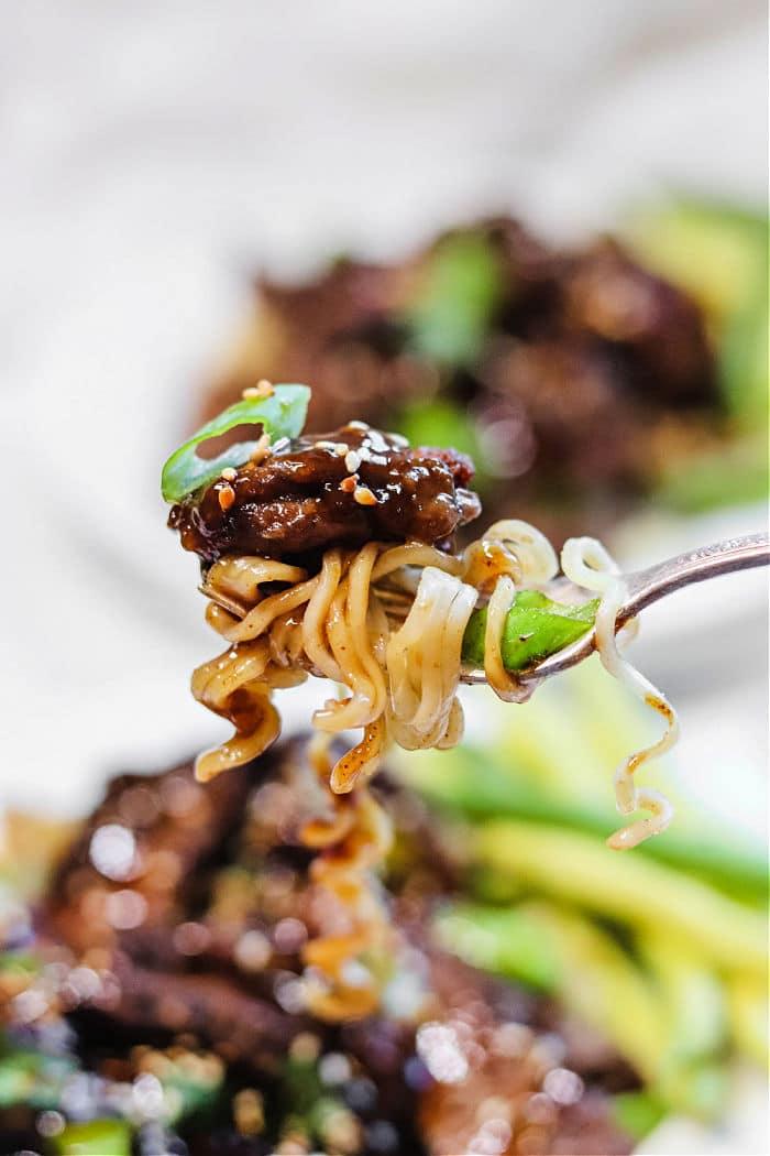 Close-up of a fork holding air fryer beef and noodles, sprinkled with sesame seeds and garnished with fresh green onions.