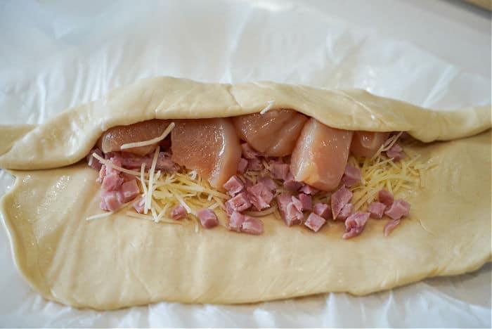 Unbaked pastry filled with diced chicken, grated cheese, and chicken pieces awaits transformation into a delicious air fryer chicken cordon bleu on parchment paper.