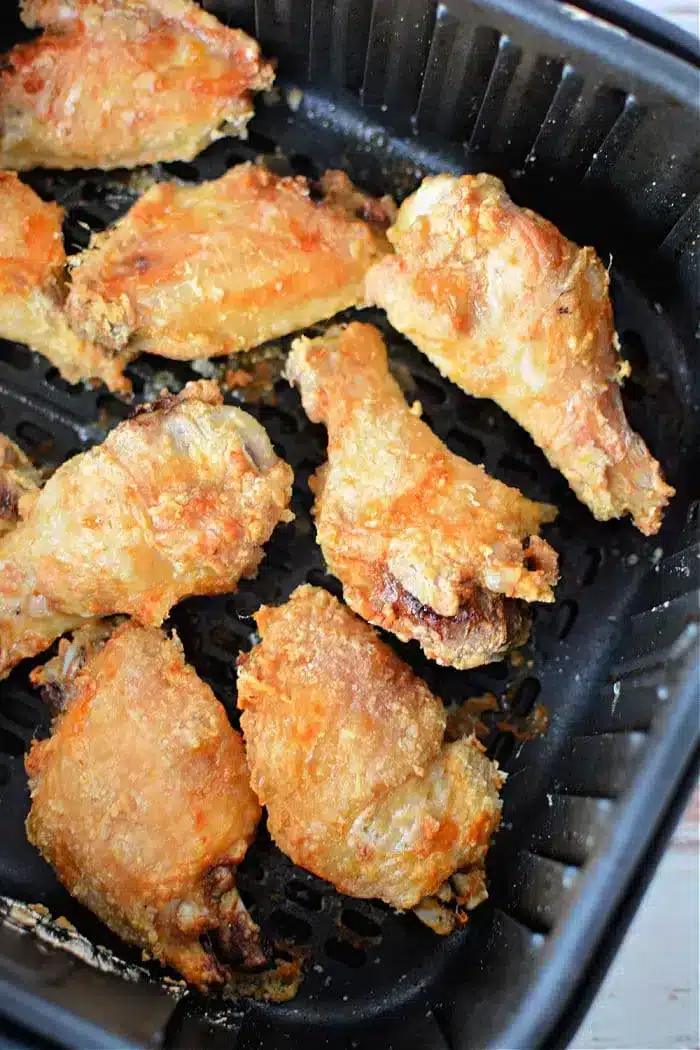 Eight pieces of crispy, golden-brown chicken wings are shown inside a black air fryer basket. The wings have a slightly uneven, textured surface, indicating they are well-cooked and well-seasoned. Thanks to the addition of baking powder, these air fryer chicken wings achieve their delightful crunch.