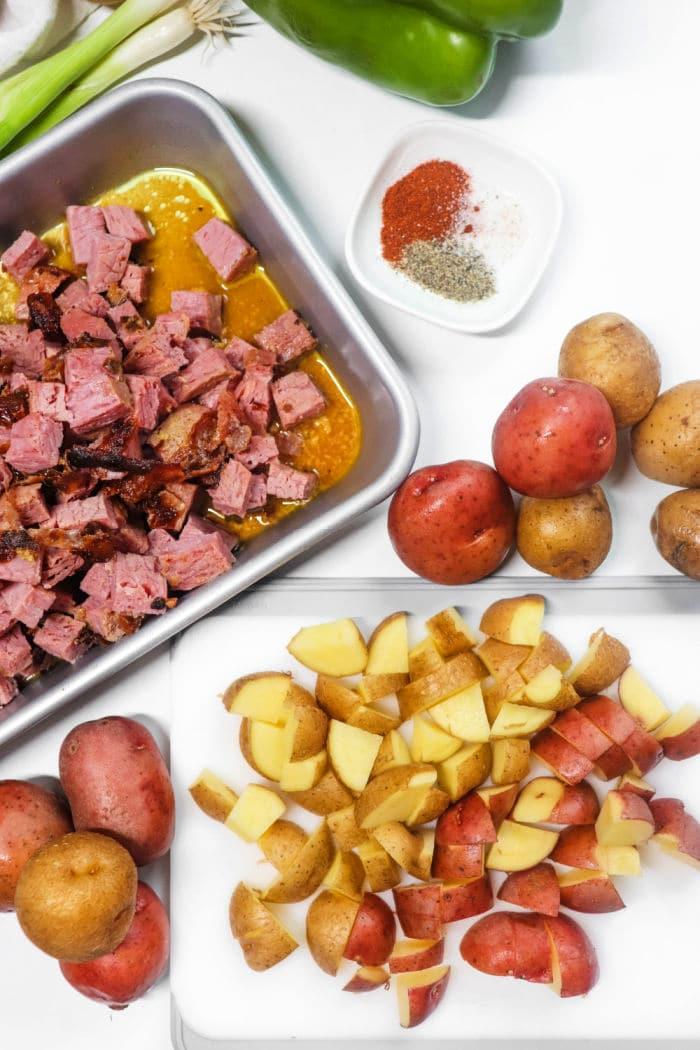 Chopped corned beef meat in a tray, diced potatoes on a cutting board, with spices and vegetables around—perfect for creating an Air Fryer Corned Beef Hash with tender red potatoes.