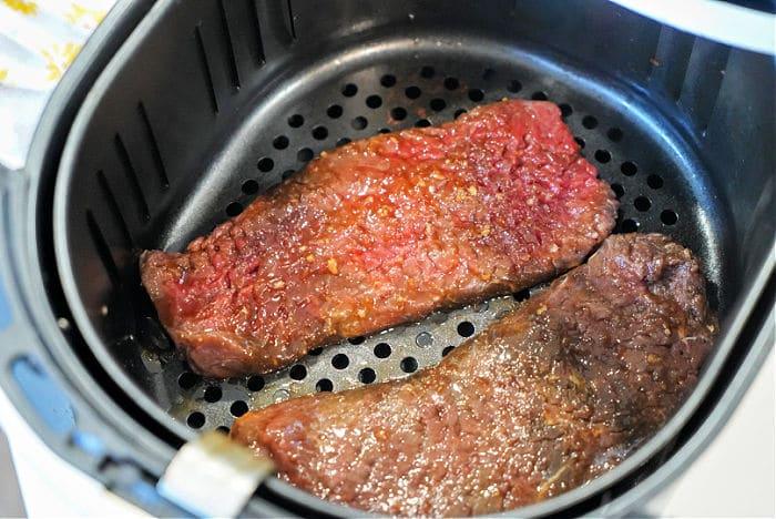 Two pieces of raw cube steak sit in an air fryer basket, ready for cooking.