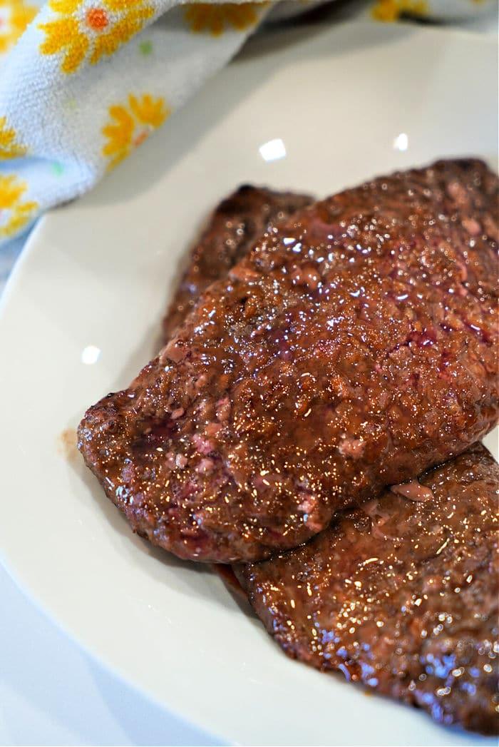 Close-up of raw minute steak slices on a white plate, with a patterned towel in the background, reminiscent of preparing air fryer cube steak.