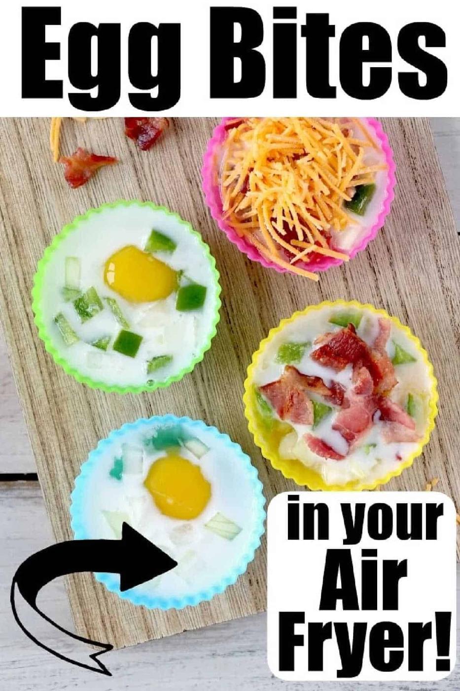 Four silicone muffin cups filled with eggs, veggies, cheese, and bacon on a wooden board, labeled air fryer egg bites.