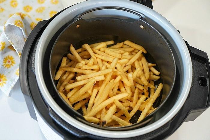Crispy French fries sit beside a yellow floral cloth, freshly golden from the air fryer. Perfectly paired with delicious ninja foodi fish and chips for a delightful meal.