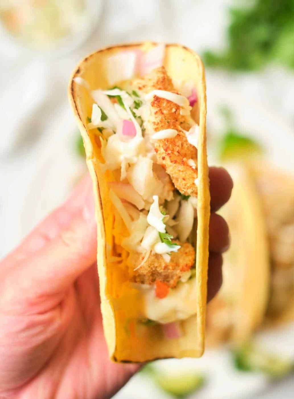 A hand holds a taco filled with crispy air fryer fish, shredded cabbage, red onion, and cilantro.