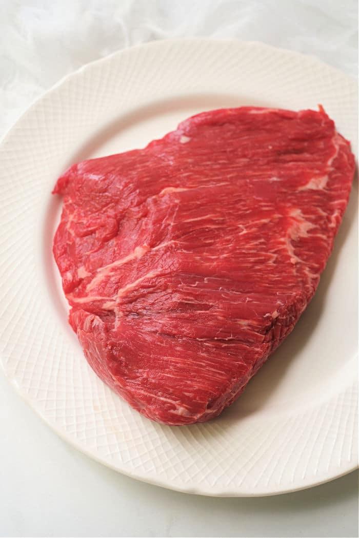 A raw flank steak rests invitingly on a white plate, just waiting to be transformed into a succulent dish in the air fryer.