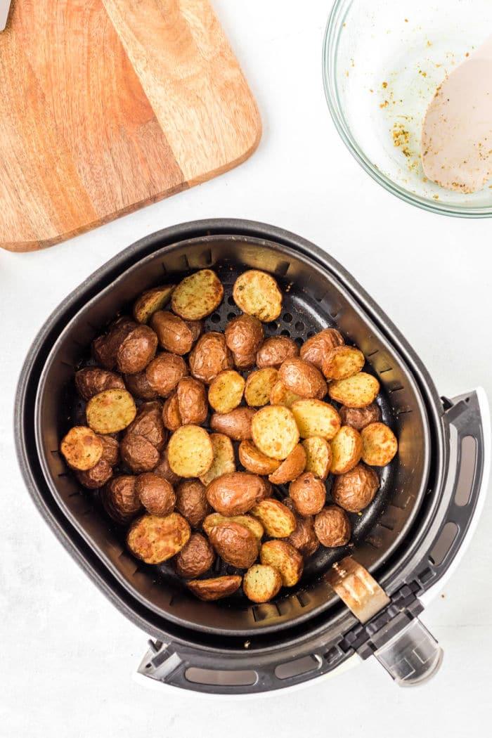 Air fryer basket with perfectly seasoned, crispy air fryer fried potatoes on a white surface.