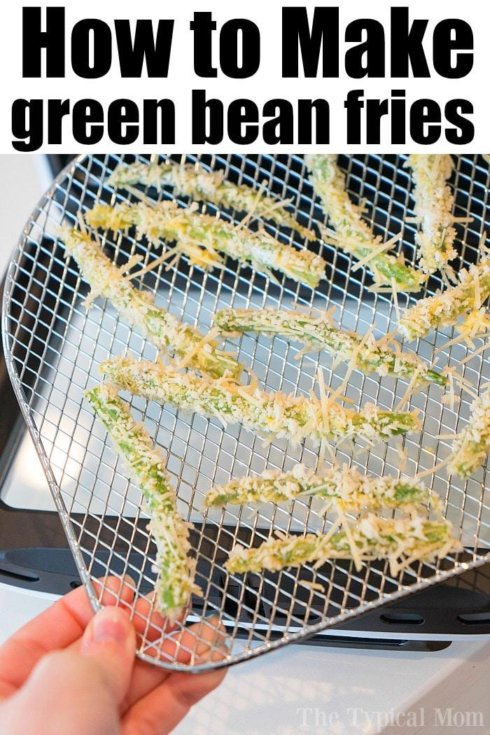 A hand holding a metal rack with breaded green bean fries, ready to crisp up perfectly in the air fryer. The text at the top reads How to Make Air Fryer Green Bean Fries.