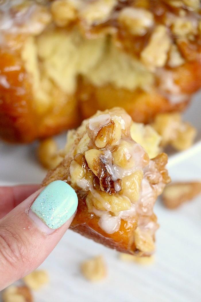 A hand with mint green nails holds a piece of glazed air fryer monkey bread creation.