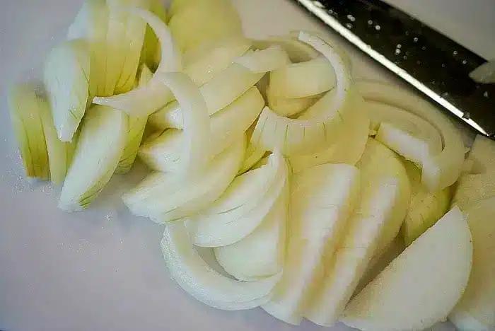 Slices of white onion on a cutting board next to a knife, ready to be transformed into crispy air fryer onions.