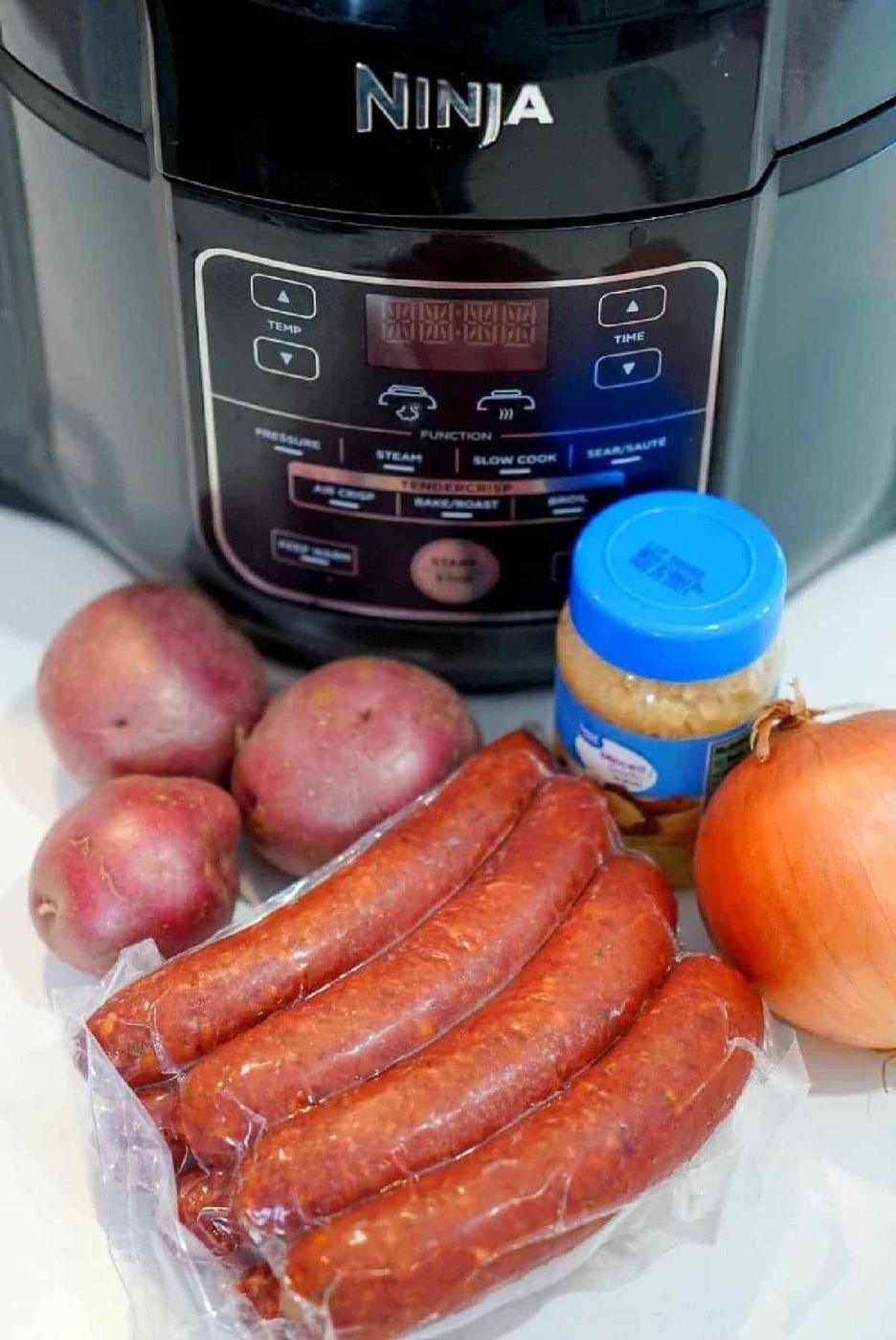 Potatoes, kielbasa sausage, an onion, and a jar of minced garlic arranged in front of a Ninja pressure cooker—perfect for making flavorful air fryer sausage meals.