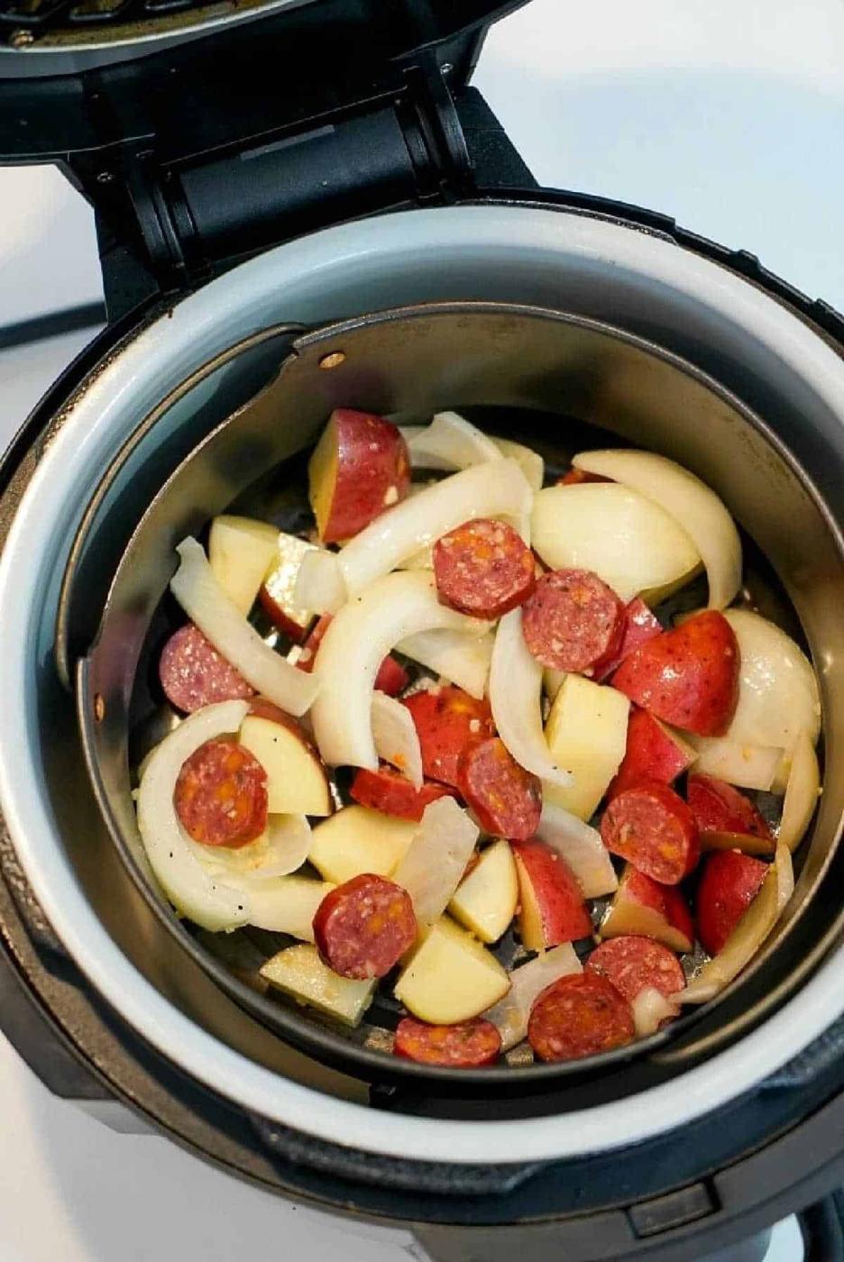 Sliced sausage, potatoes, and onions are arranged in an electric pressure cooker, similar to how you'd prep for tasty air fryer sausage recipes—ready to be cooked to perfection.