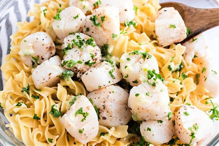 A bowl of pasta topped with air fryer scallops, garnished with parsley.