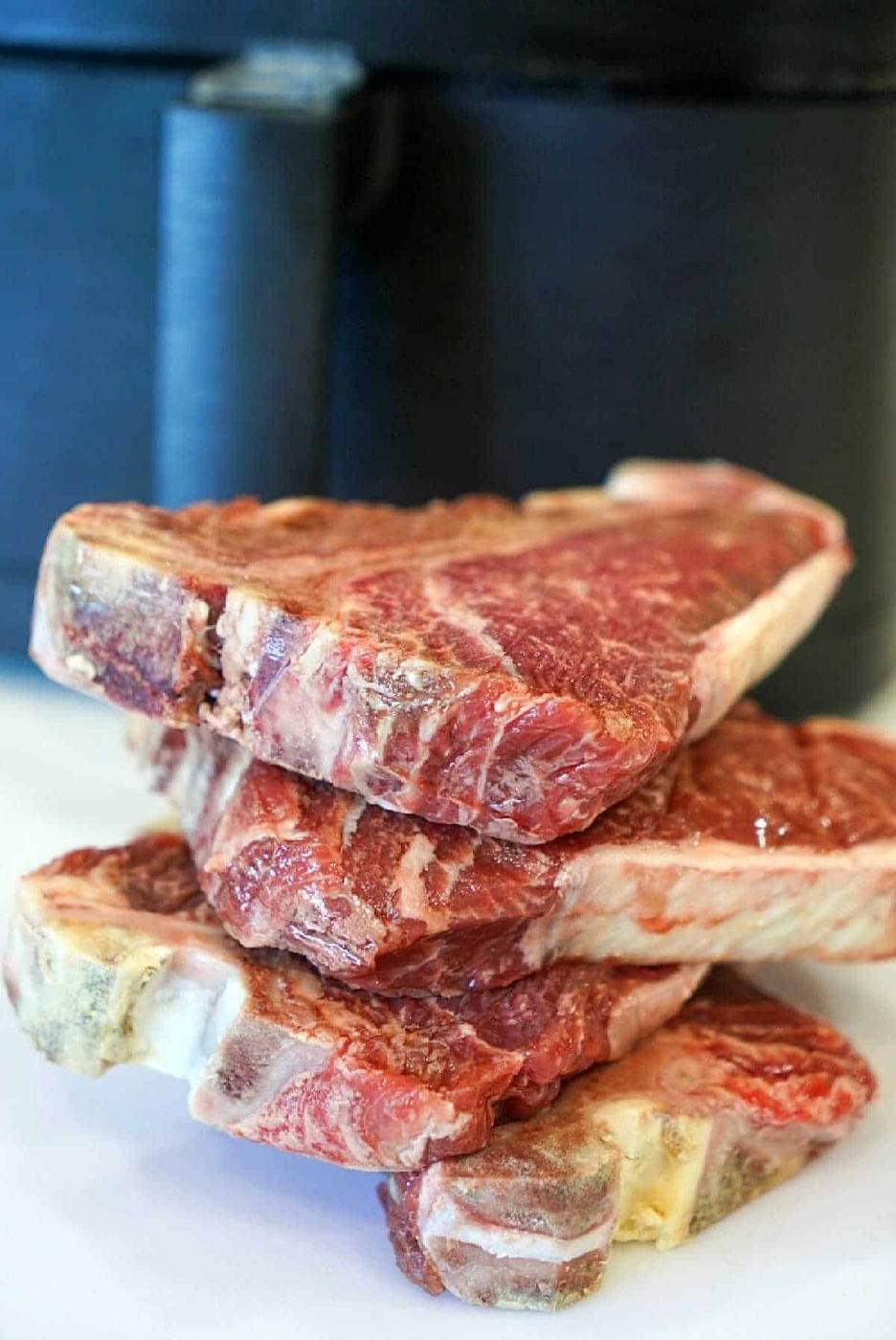 Four frozen raw steaks stacked on a white surface with a black appliance in the background—perfect for making juicy air fryer steak bites.