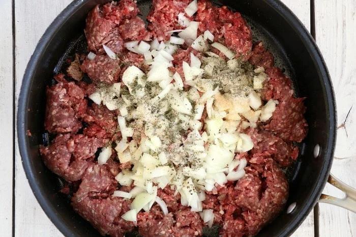 Ground beef, chopped onions, and spices in a black skillet are prepped for air fryer stuffed peppers, ready to be cooked on a wooden surface.