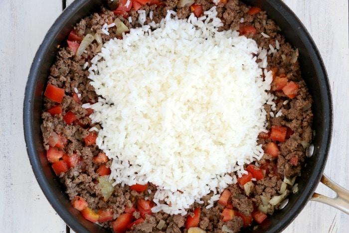A skillet with cooked ground beef, chopped tomatoes, and a mound of white rice on top—perfect ingredients for making air fryer stuffed peppers.
