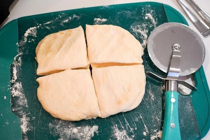 Homemade flour tortilla recipe in its simplicity, is cut into four pieces on a green cutting board, with a pizza cutter resting beside it.