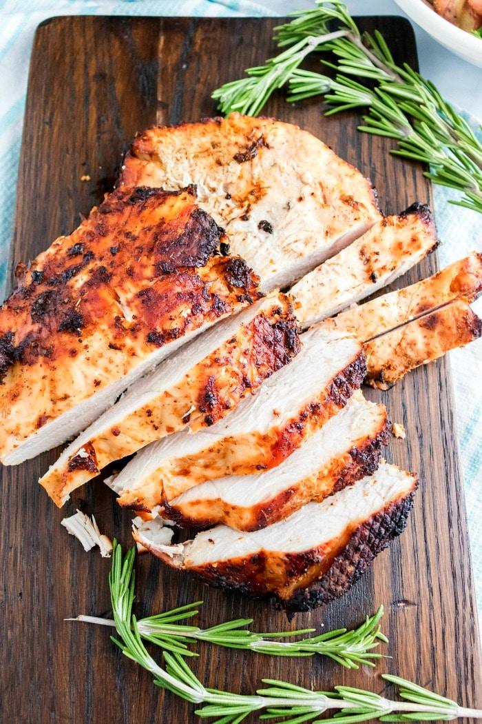 Sliced roasted turkey breast on a wooden cutting board, garnished with sprigs of rosemary, brings to mind the juicy tenderness of air fryer turkey breast.