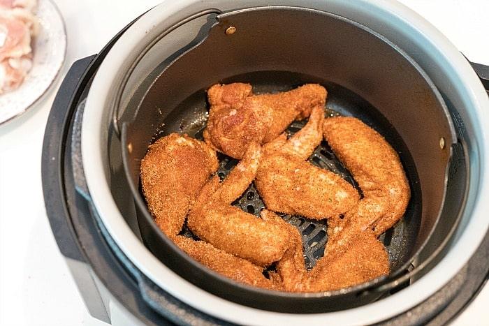 In an enticing air fryer wings recipe, chicken wings seasoned with spices rest in the air fryer basket, ready to be cooked to perfection. The air fryer stands proudly on the kitchen counter, with a glimpse of a plate holding raw chicken visible in the background.