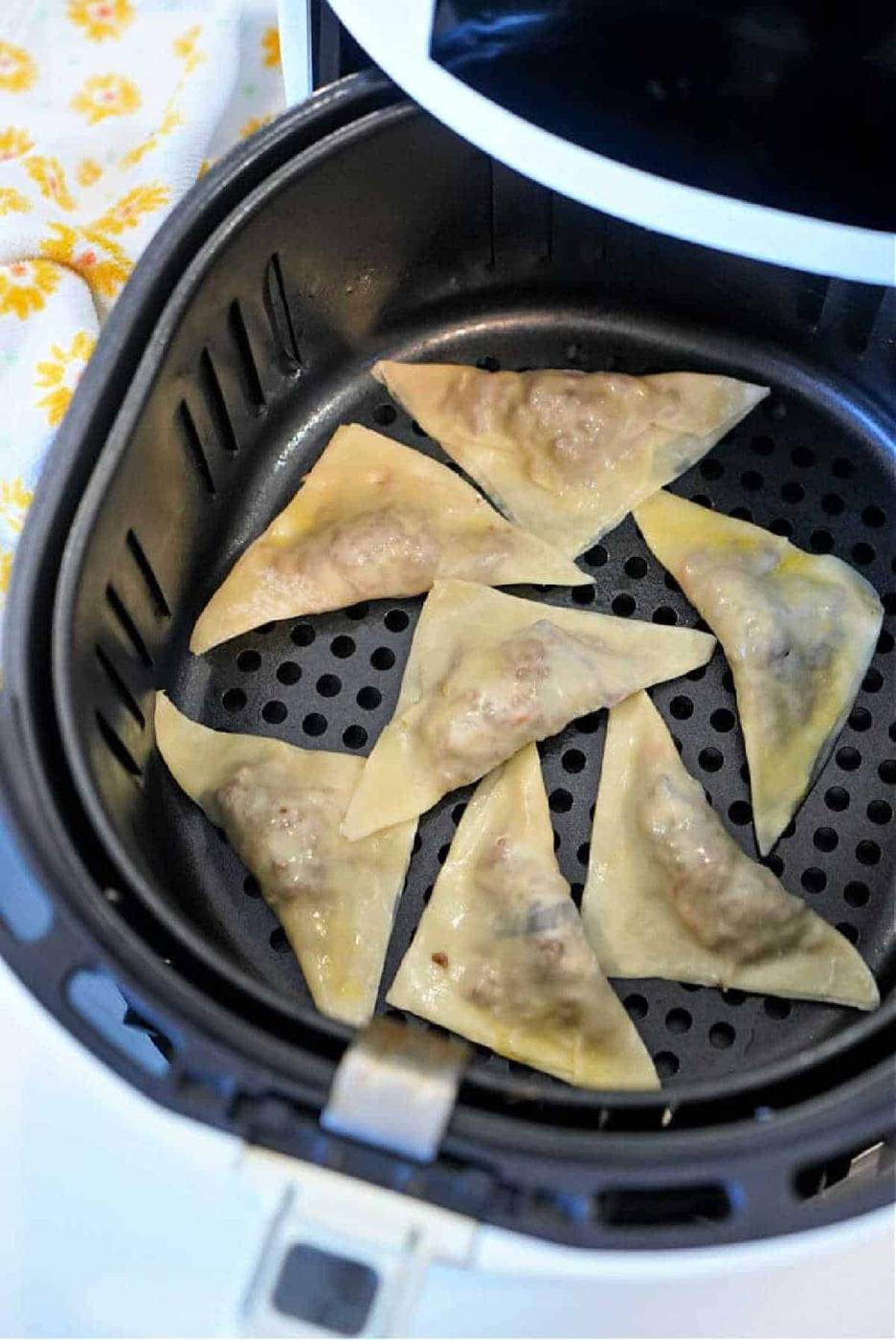 Eight uncooked air fryer won tons are arranged in a single layer inside an open air fryer basket.