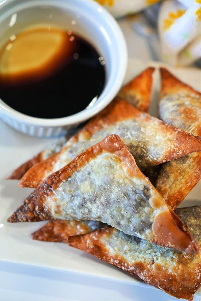 Crispy air fryer won tons stacked on a plate next to a small bowl of soy sauce with a lemon slice.