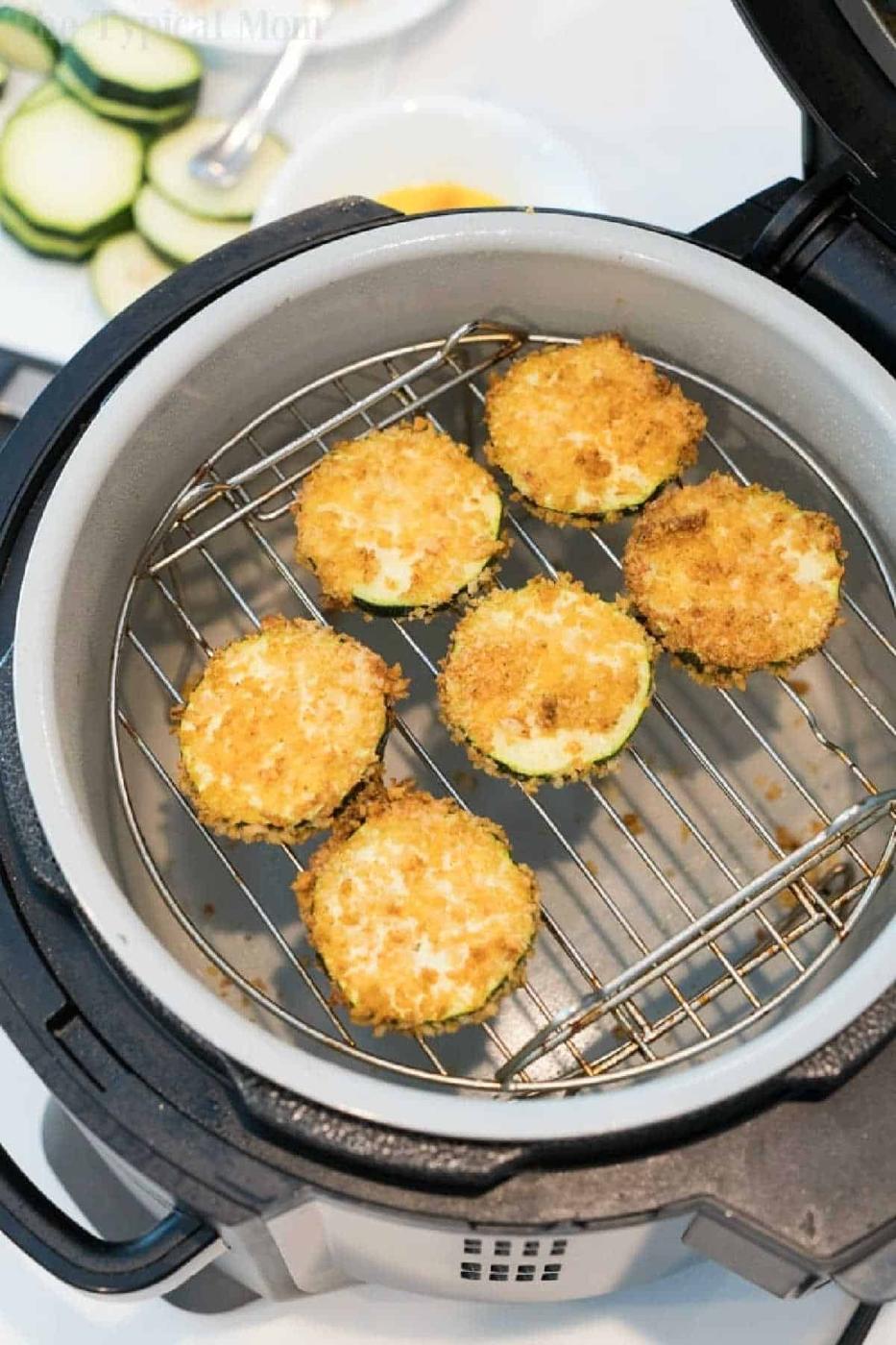 Six breaded air fryer zucchini chips are arranged on a rack inside an air fryer, ready to be cooked.