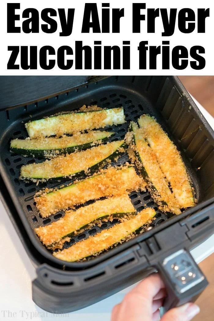 A close-up of air fryer zucchini fries coated in breadcrumbs cooking in an air fryer basket. The text at the top reads "Easy Air Fryer zucchini fries," and a hand is shown holding the air fryer drawer.