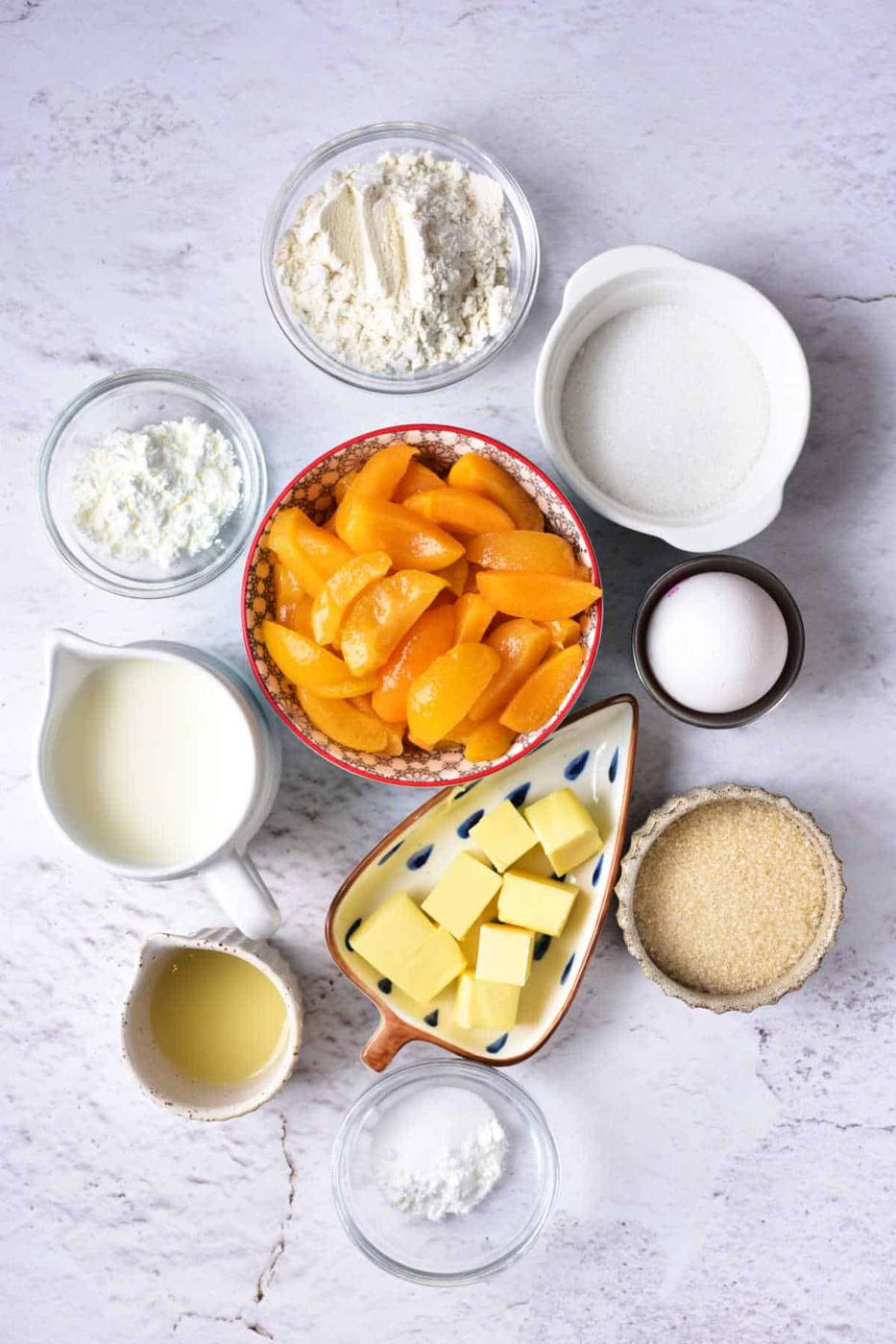 Ingredients laid out for a delightful apricot cobbler recipe, including juicy peaches, ripe apricots, flour, sugar, butter, milk, and eggs.