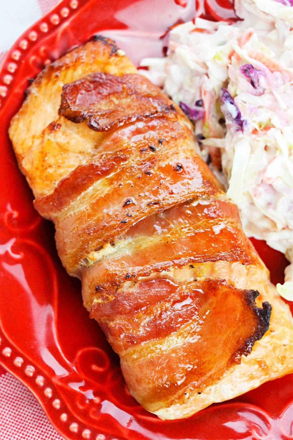 Bacon Wrapped Salmon fillet served with coleslaw on a vibrant red plate.