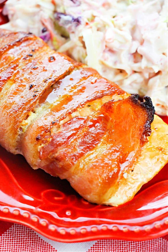 Bacon-wrapped salmon slice shares the spotlight with creamy coleslaw on a vibrant red plate, tempting even bacon-wrapped salmon enthusiasts.