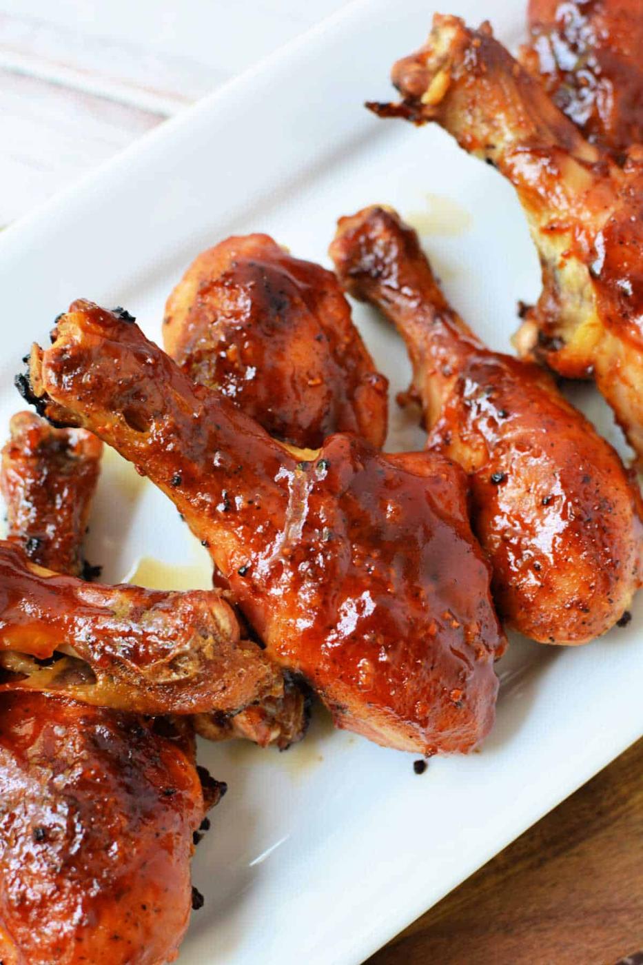 Glazed barbecue chicken drumsticks, prepared from baked frozen chicken legs, are artfully arranged on a white rectangular plate.