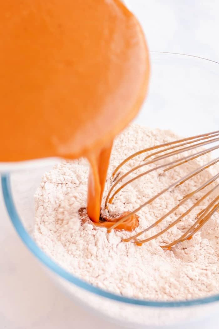 pumpkin being poured into a bowl of dry ingredients with a whisk, creating the perfect base for baked pumpkin donuts.