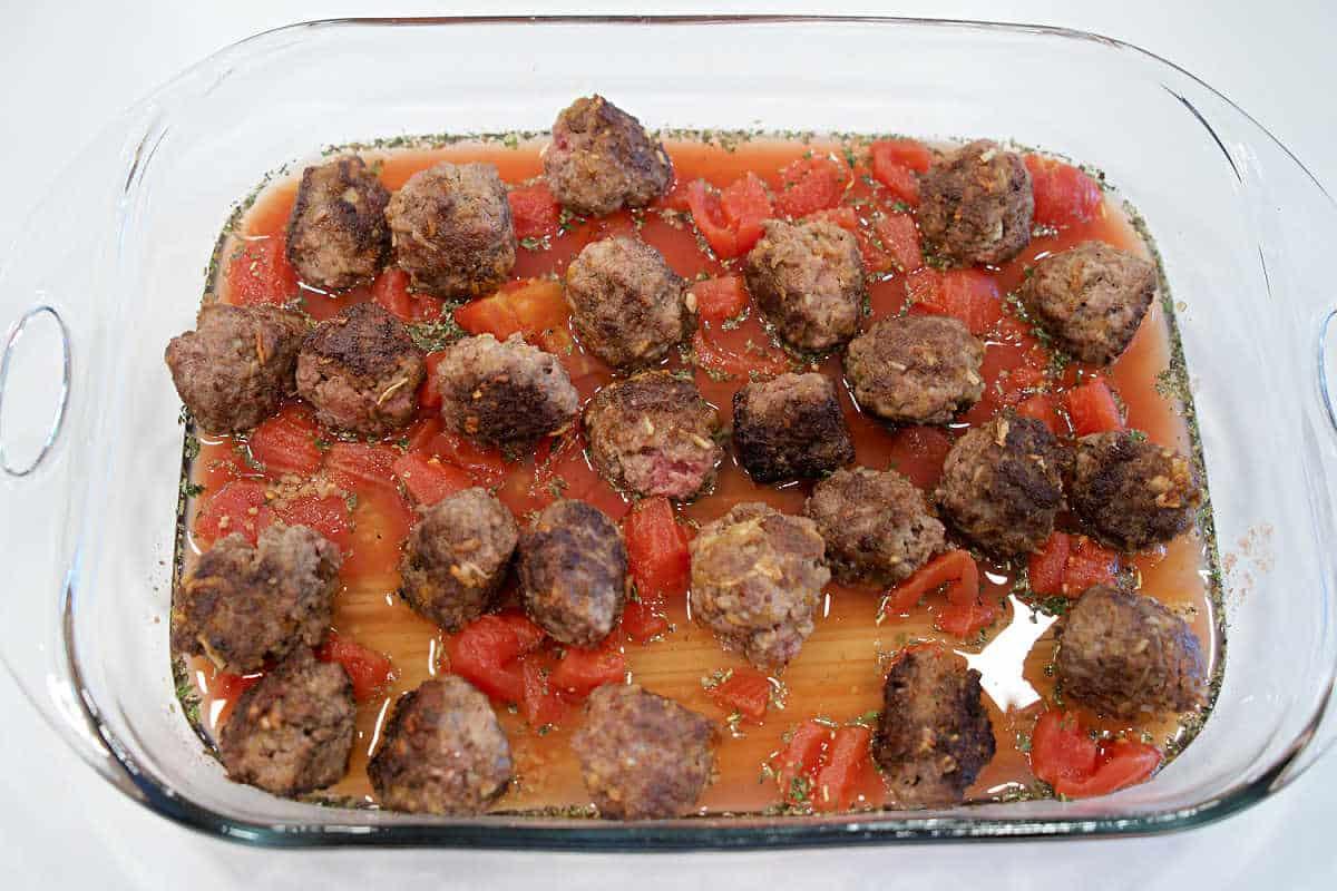 Baking dish with meatballs, diced tomatoes, sauce, and herbs, arranged over uncooked lasagna noodles for a delicious twist on Baked Spaghetti with Meatballs.
