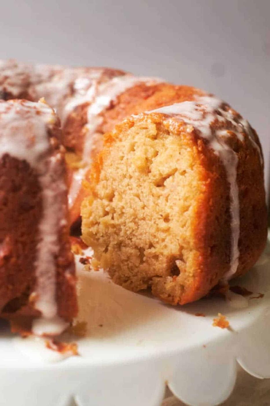 A sliced Banana Bread Bundt Cake with white icing drizzled on top, displayed on a white cake stand.