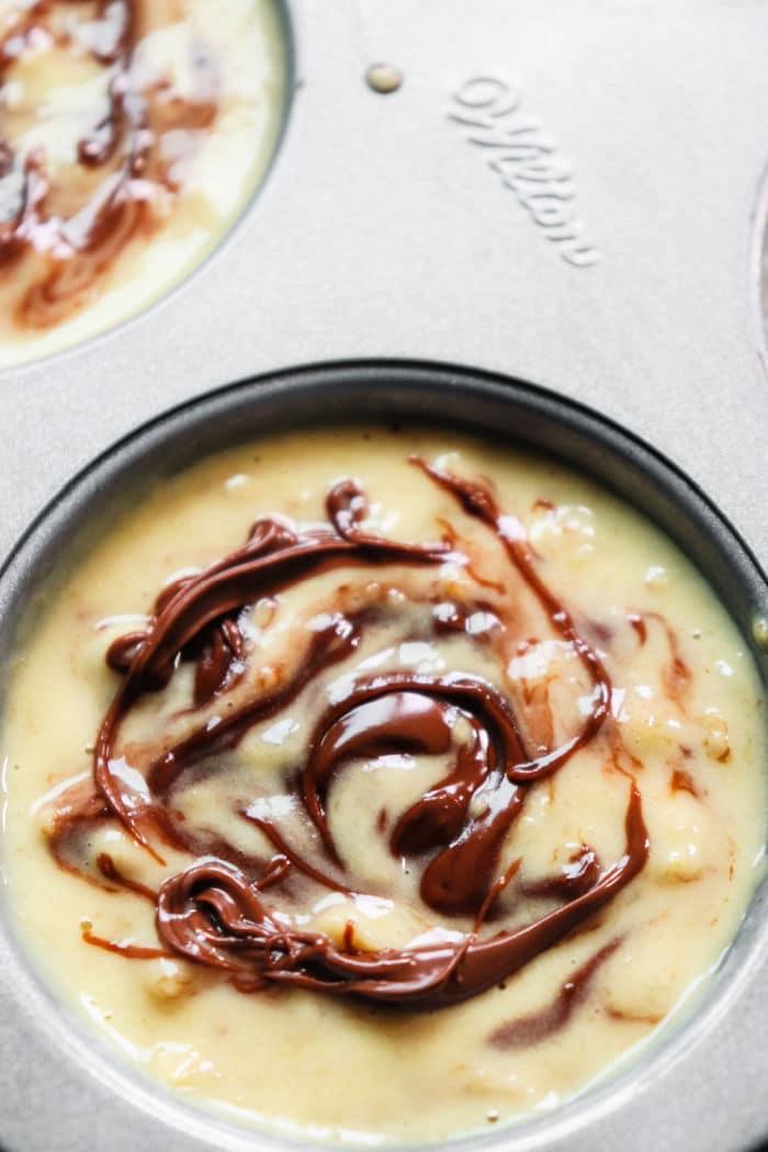 Close-up of banana muffin batter with luscious Nutella swirls in a baking tin.