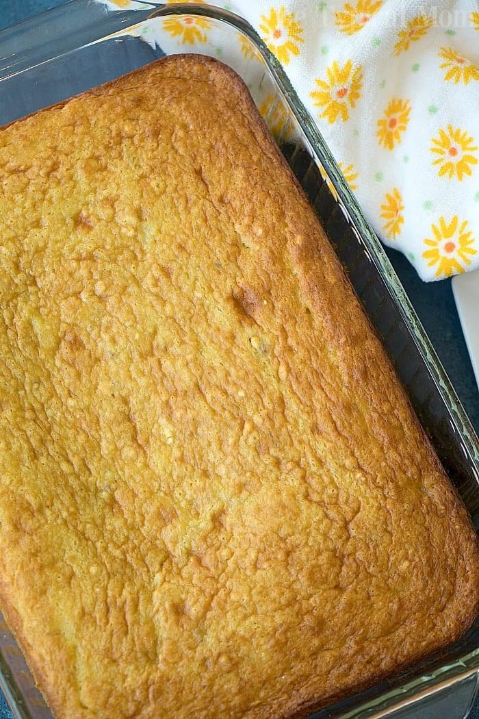 Golden baked banana pudding cake in a glass dish next to a floral yellow and white napkin, reminiscent of a cozy cake mix afternoon.