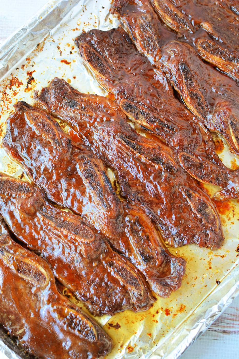 Rows of glazed, cooked beef riblets rest on a foil-lined baking sheet—perfect for anyone searching for a savory beef riblets recipe.