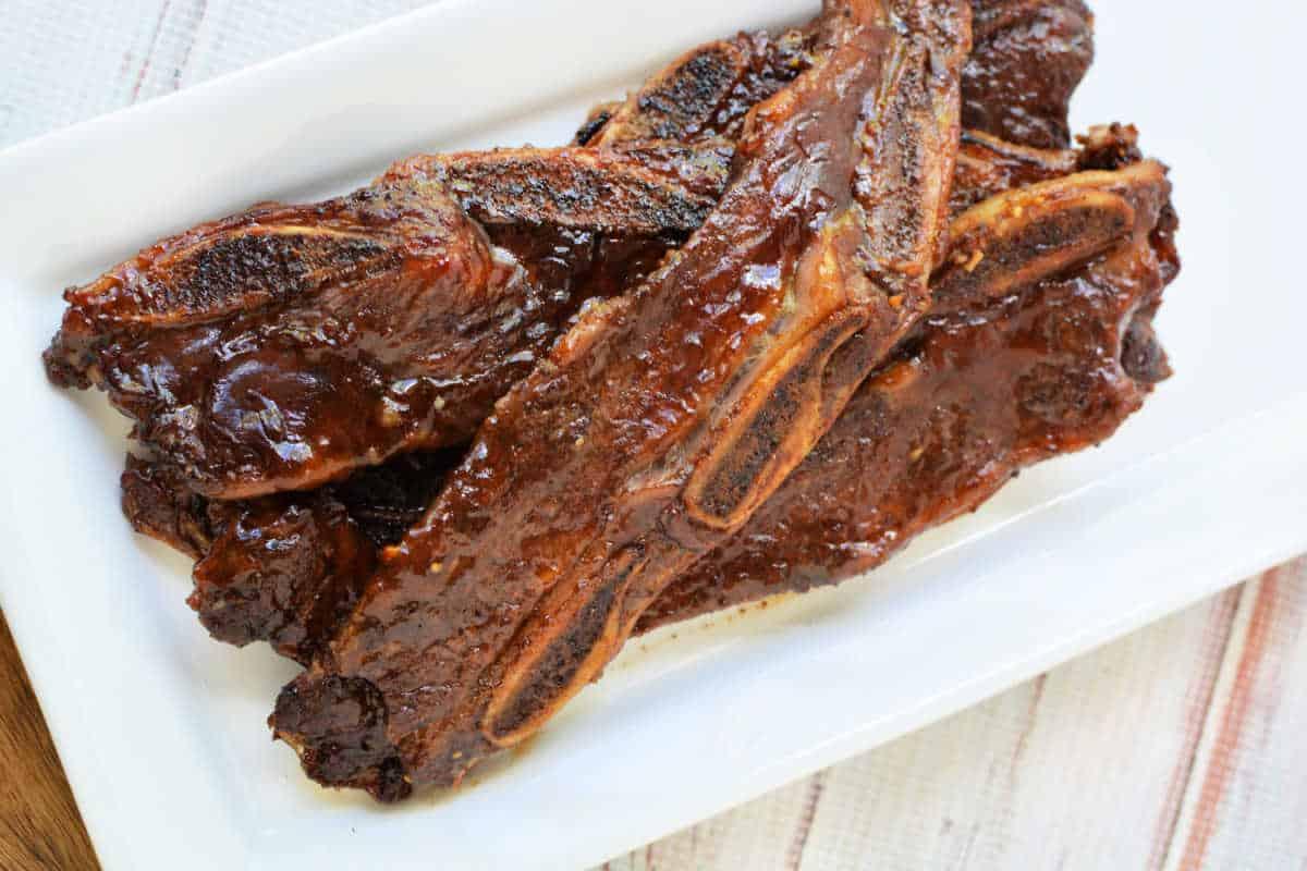Grilled beef riblets with a shiny glaze, served on a rectangular white plate—a mouthwatering beef recipe perfect for any occasion.