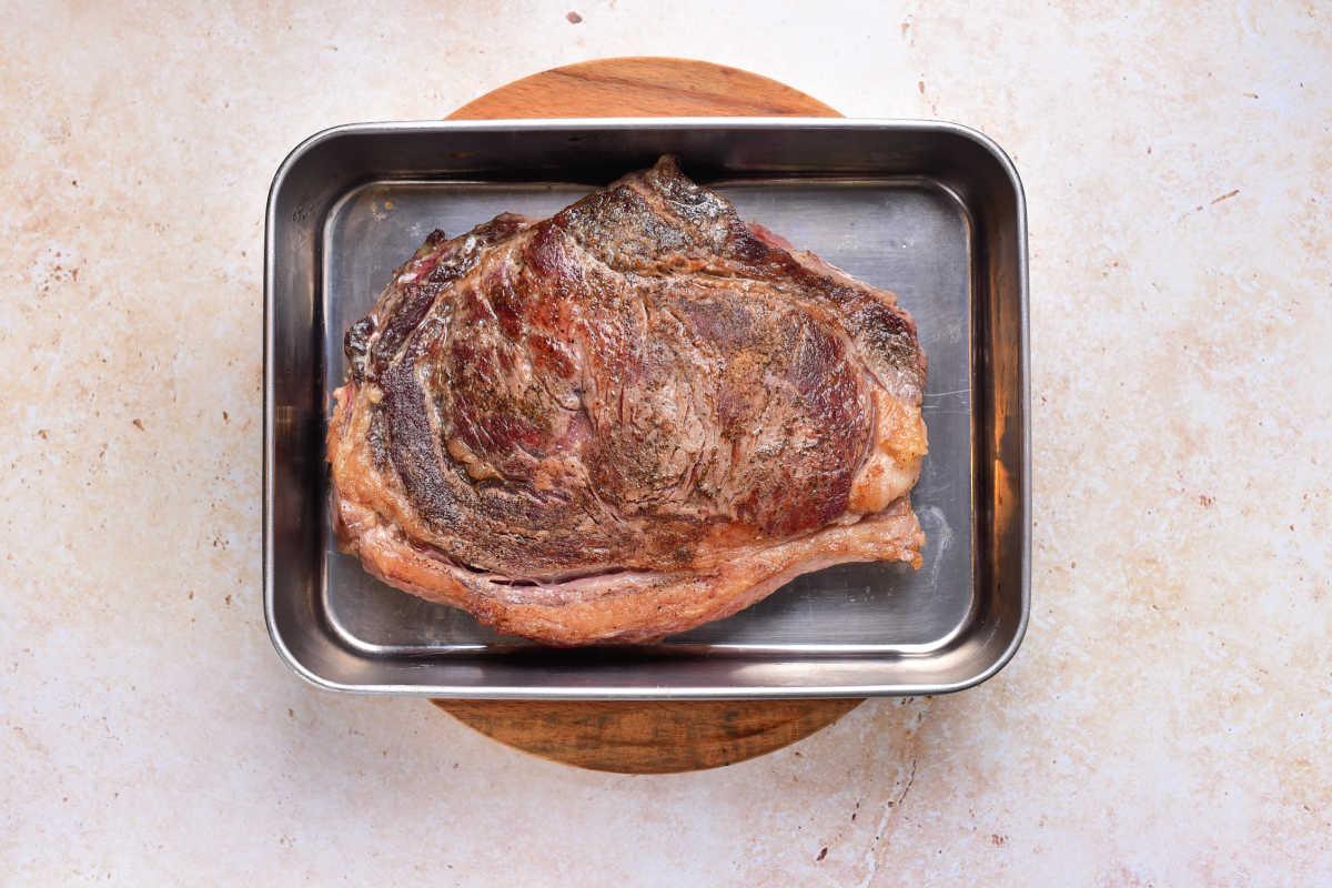 Cooked strip steak in a metal roasting pan on a round wooden board, viewed from above—perfect inspiration if youre wondering how to cook beef strip steak in the oven for juicy and delicious results.
