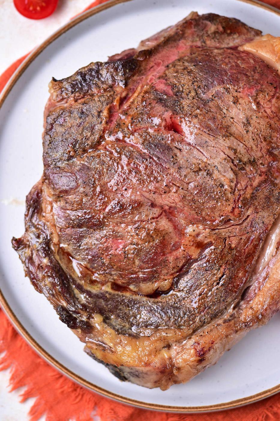 A cooked steak with a seared crust, served on a white plate with an orange placemat underneath—perfect inspiration if you’re wondering how to cook beef strip steak in the oven for a similar juicy result.