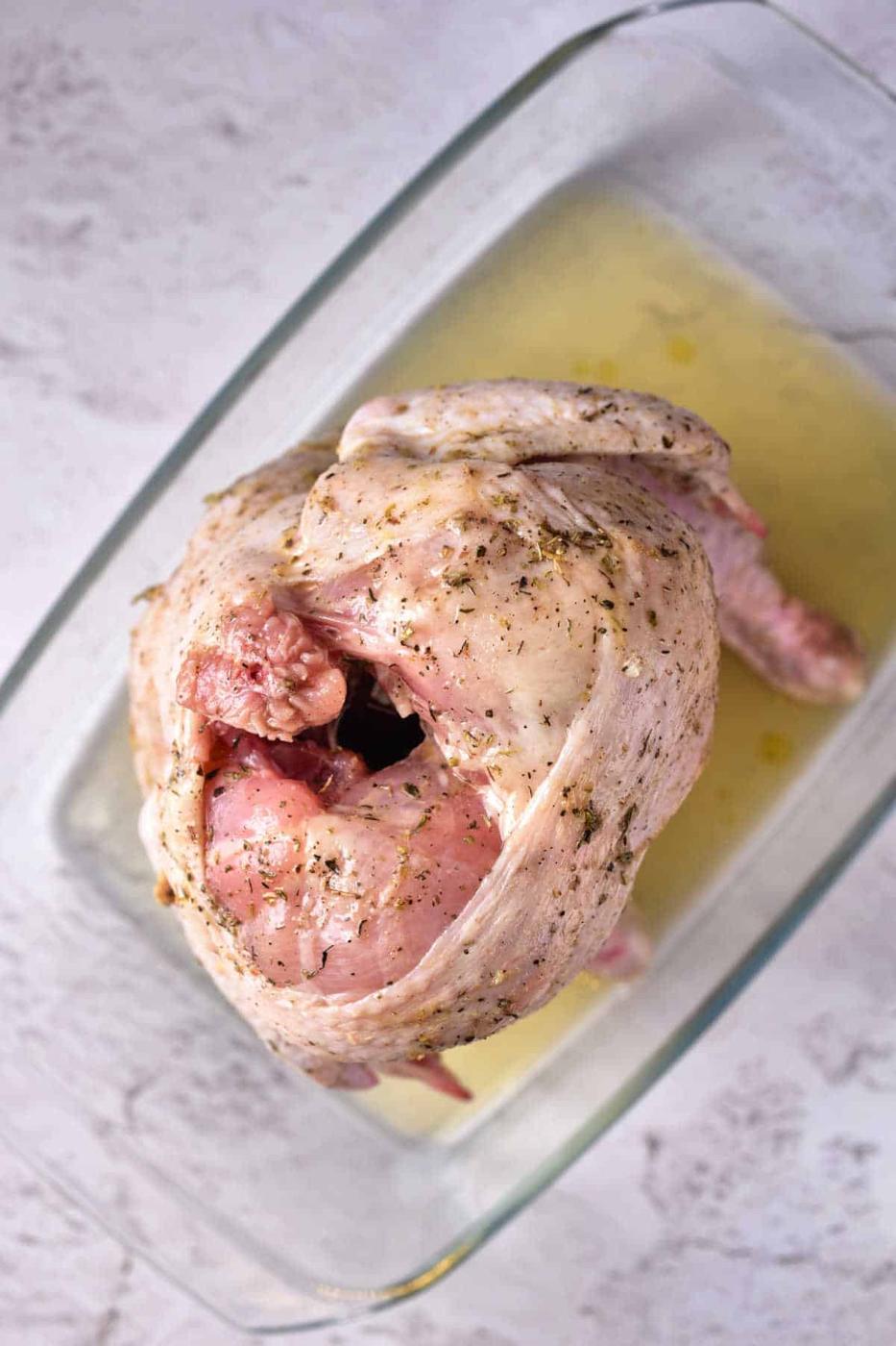 Raw seasoned Beer Can Chicken in the Oven, sits ready in a glass baking dish on a light surface.