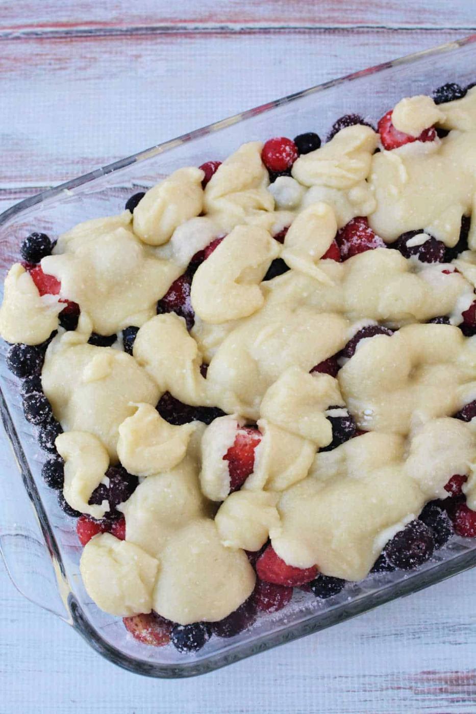 A glass baking dish filled with mixed berries and blobs of unbaked dough on top, this Berry Cobbler with Cake Mix is ready to be baked for a simple, delicious dessert.