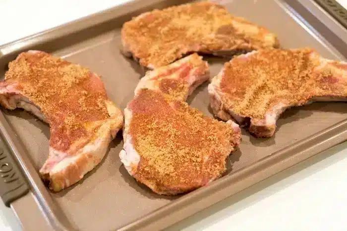 Four seasoned raw pork chops on a baking sheet, ready to become the best baked pork chops for your next delicious meal.