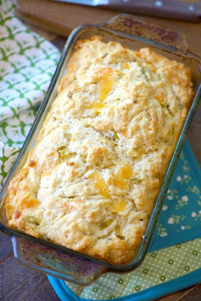A loaf of delicious beer bread, reminiscent of the best beer bread recipe, sits invitingly in a glass baking dish, with floral and teal cloths underneath.